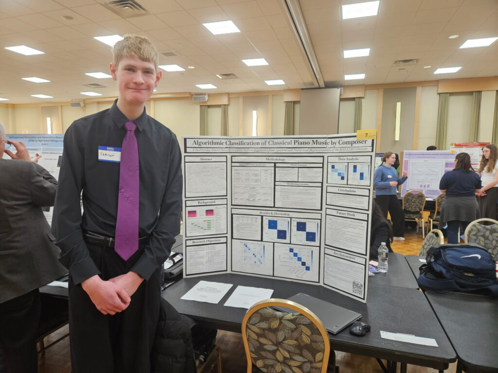 Young man in a black shirt and purple tie stands beside a science-fair poster about algorithmic classification of classical piano music.